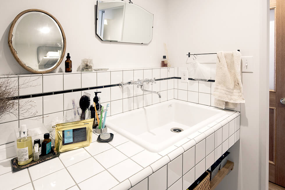 白×黒のタイルがスタイリッシュな洗面台。アンティークの鏡、アナログタイプの蛇口ともお似合い。娘たちのことを考えて、ちょっと広めに造作